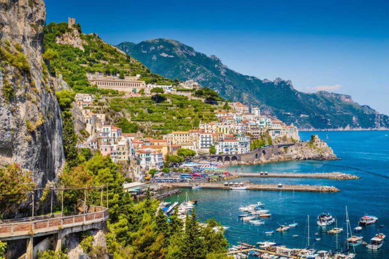 Colourful hillside town of Amalfi on Italy’s southern coast, a stunning once-in-a-lifetime travel destination with boats in the harbour and dramatic cliffs rising above the sea.