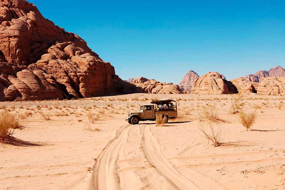 7 Best Wadi Rum Jeep Tours, Jordan: Choosing the Best 4x4 Wadi Rum Experience 5 A jeep tour with a tourist on board is seen in the middle of Wadi Rum desert, under a clear blue sky