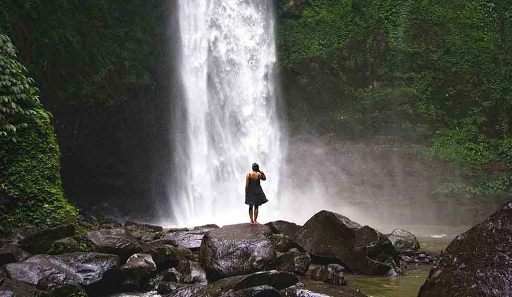 Girl in a black dress stood in front of Nungnung Waterfall in Bali