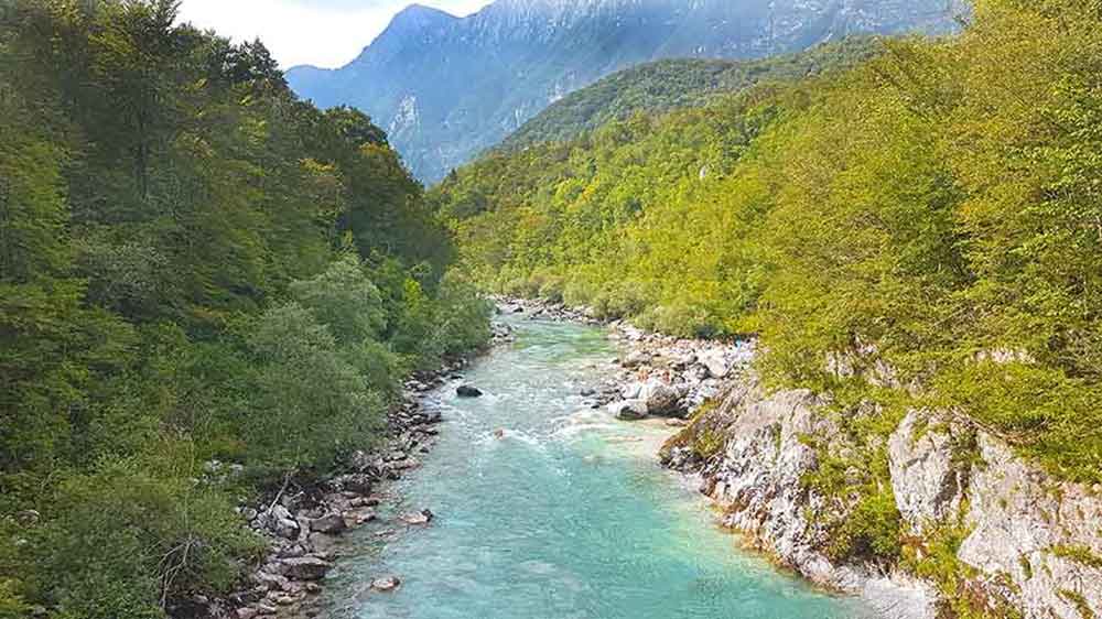 A Soca River in Slovenia featuring turquiose and non-stop over flowing of water surrounded by large rocks and trees