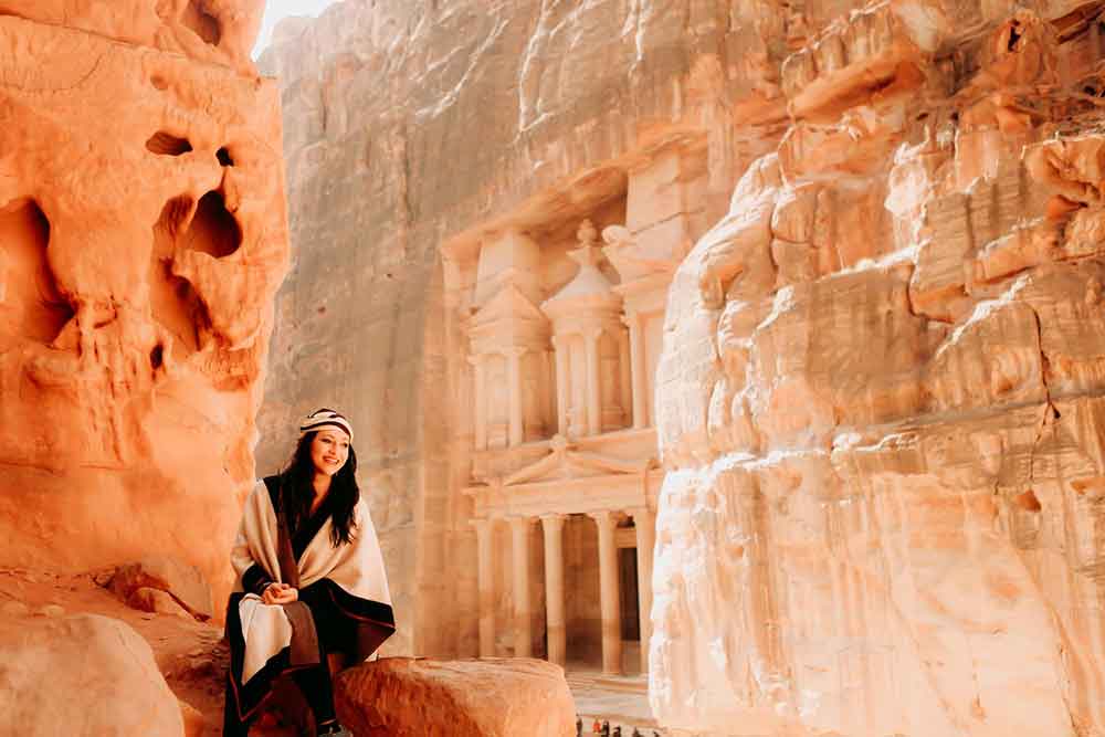 A woman sitting on the stone wearing a headscarf and shawl over her shoulders at Treasury, Petra, Jordan