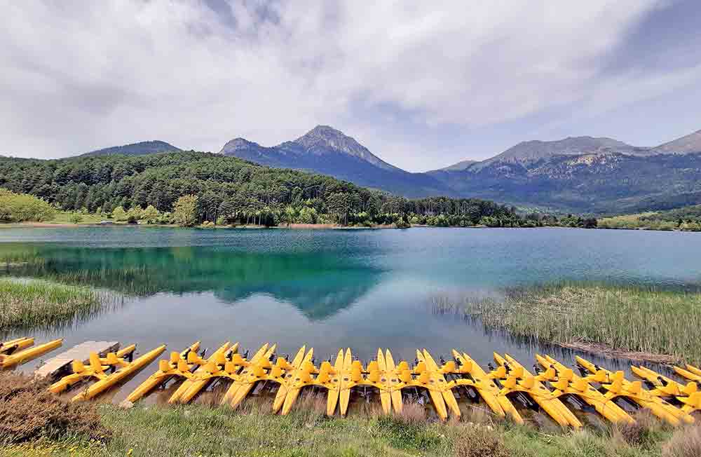 Large blue lake with mountains in the background and kayaks in the foreground.