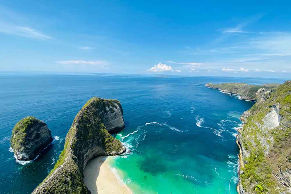 An aerial view of the Kelingking Beach at Nusa Penida with a T-rex shape of rock formation, blue water and white sand