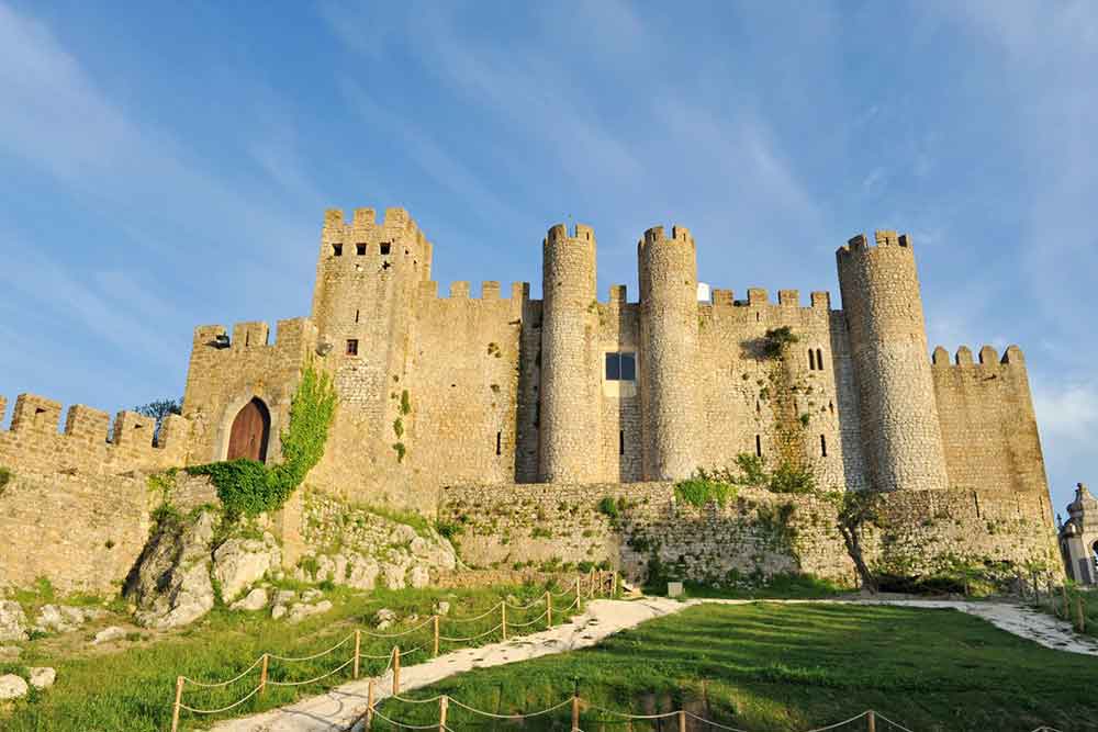 Óbidos Castle is perched atop a hill and surrounded by medieval walls adorned with crenellated battlements.