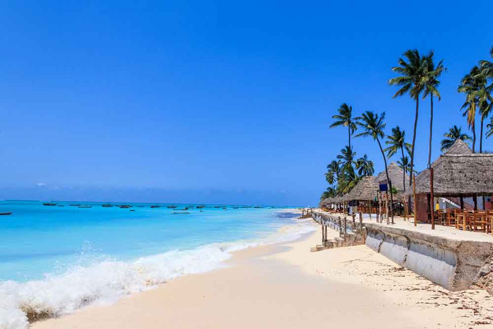 33 Best Hidden Coves and Secluded Beaches Around the World 4
Nungwi Beach in Tanzania offers a captivating view of its pristine white sands meeting the blue turquoise waters, adorned with nipa huts and palm trees along the shoreline.
