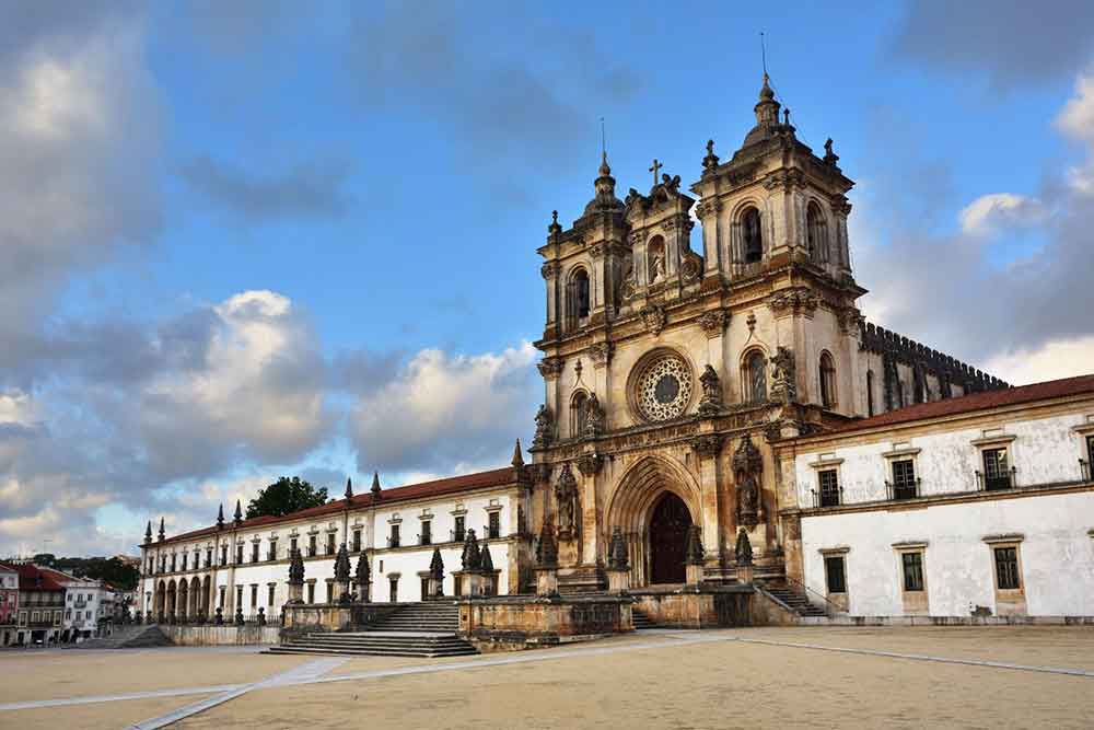 Monasterio De Alcobaca features pointed arches, bell tower and elegant brown wall with a rose window carved in circular window situated above the entrance