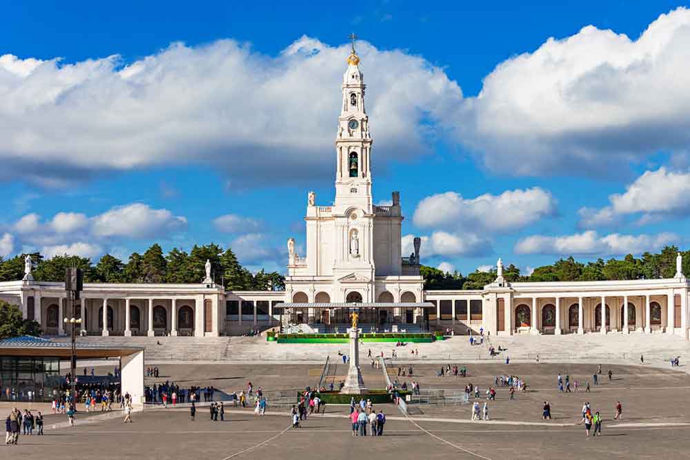 Sanctuary of Our Lady of Fatima features open spaces with a tall sanctuary standing at the center, all under a sunny sky.