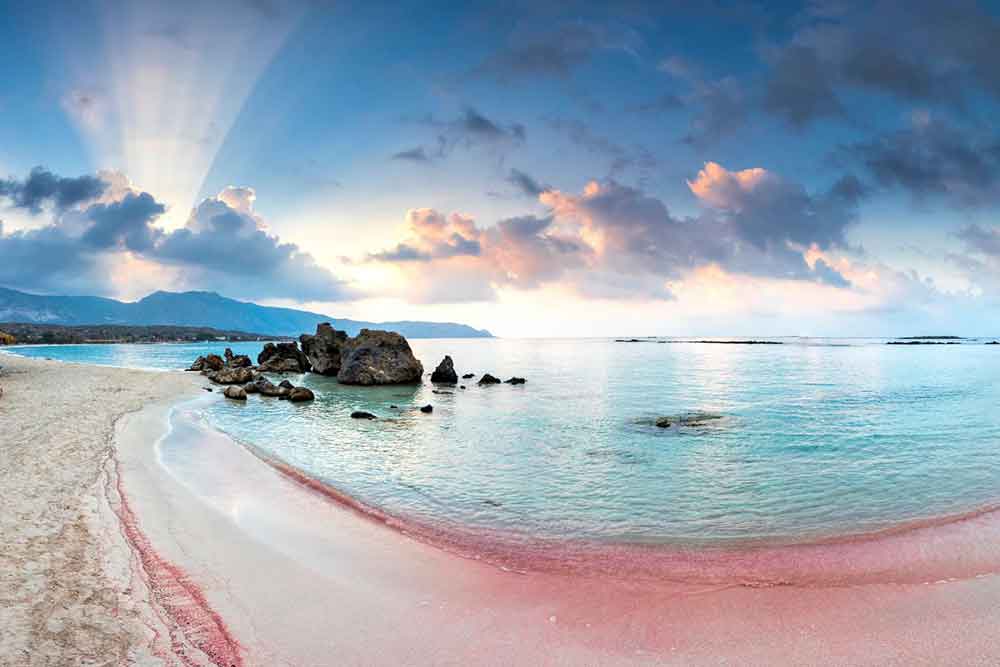 33 Best Hidden Coves and Secluded Beaches Around the World 5 Elafonissi Beach in Greece showcasing its pink sand meeting the blue water with large rocks on the side of the shoreline
