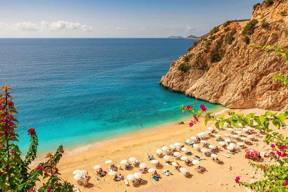 33 Best Hidden Coves and Secluded Beaches Around the World 6 An aerial view of the Kaputas Beach in Turkey showcasing a numerous umbrella stands at the shoreline, blue turquoise water and a large steep rock formation on the side