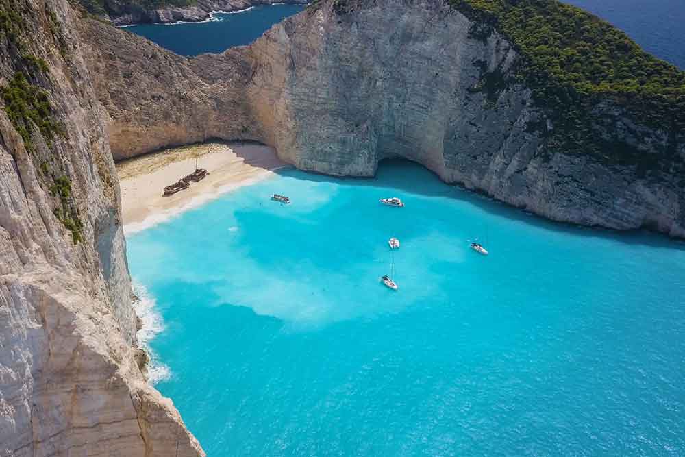 33 Best Hidden Coves and Secluded Beaches Around the World 7 Navagio Beach in Greece surrounded by steep cliffs with a broken ship parked at the end of the shoreline
