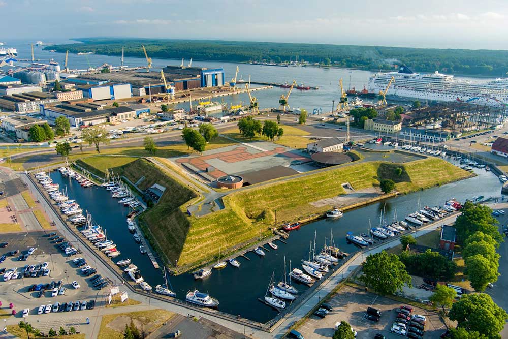 An aerial view of the Klaipeda Castle remains in Lithuania shows them surrounded by a green lawn, a lake, and boats.