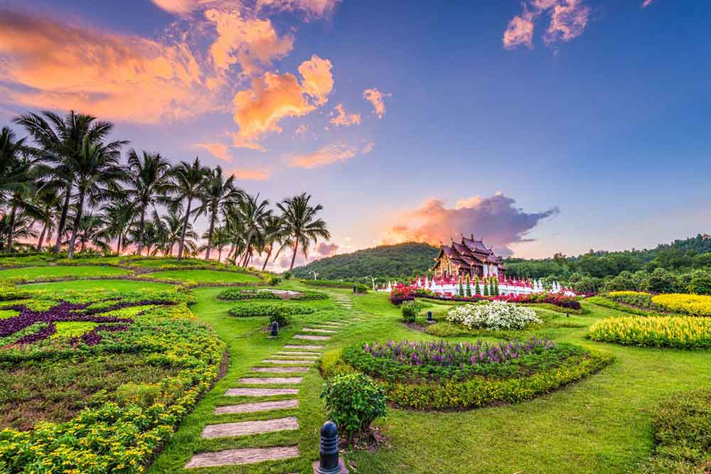 A temple with multi-tiered roofs stands in Chiang Mai, Thailand, surrounded by a well-manicured garden, lawn, and palm trees.