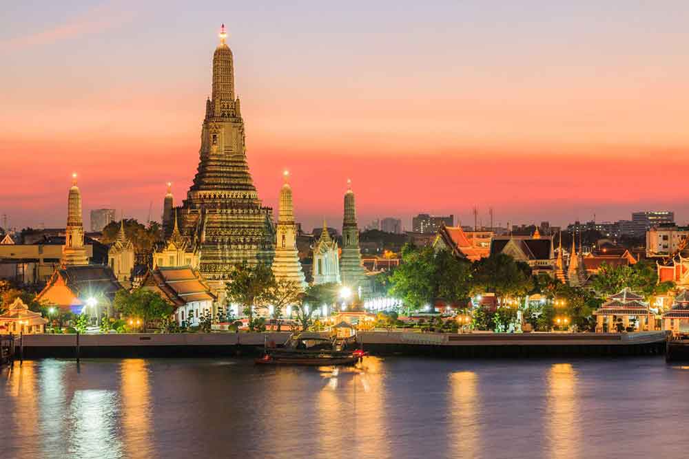 Wat Arun in Bangkok, one of the temple in Thailand, features a central large spire and four smaller spires, illuminated by lights at night, with a riverside view.