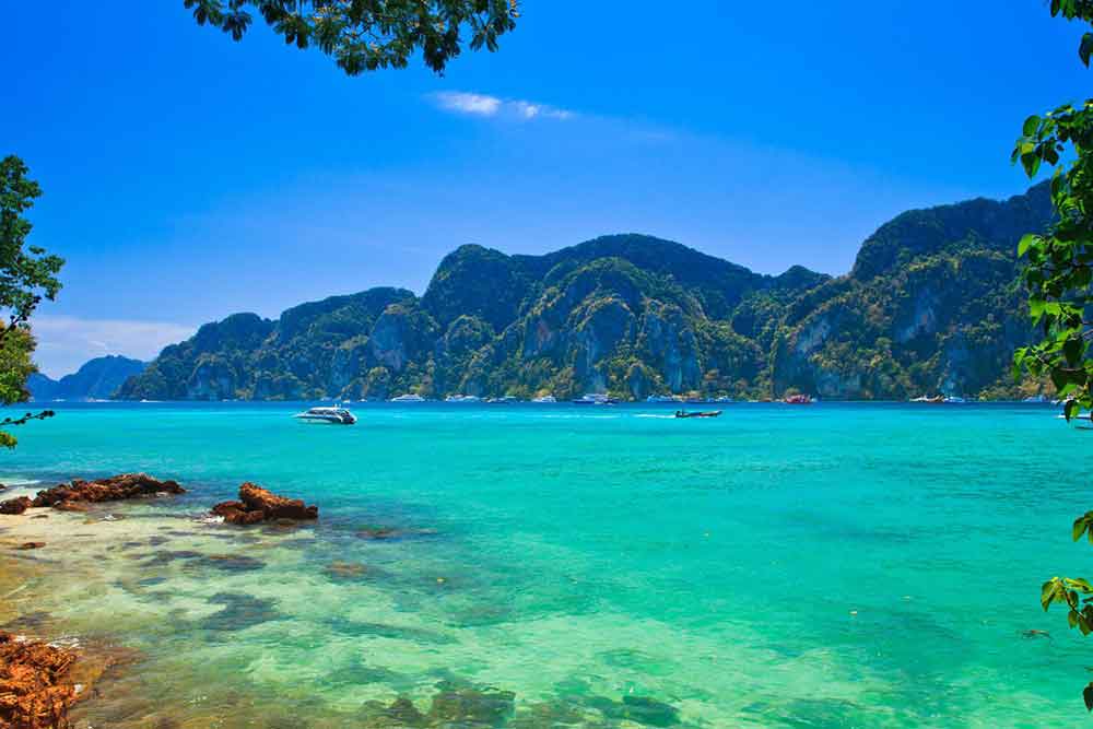 Phi Phi Island in Thailand showcases its natural beauty with crystal-clear waters and towering, steep rock mountains in the background