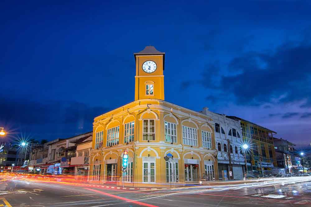 Streets at Phuket Old Town in Thailand come alive at night, featuring a charming yellow building at the corner and a prominent clock tower at the center