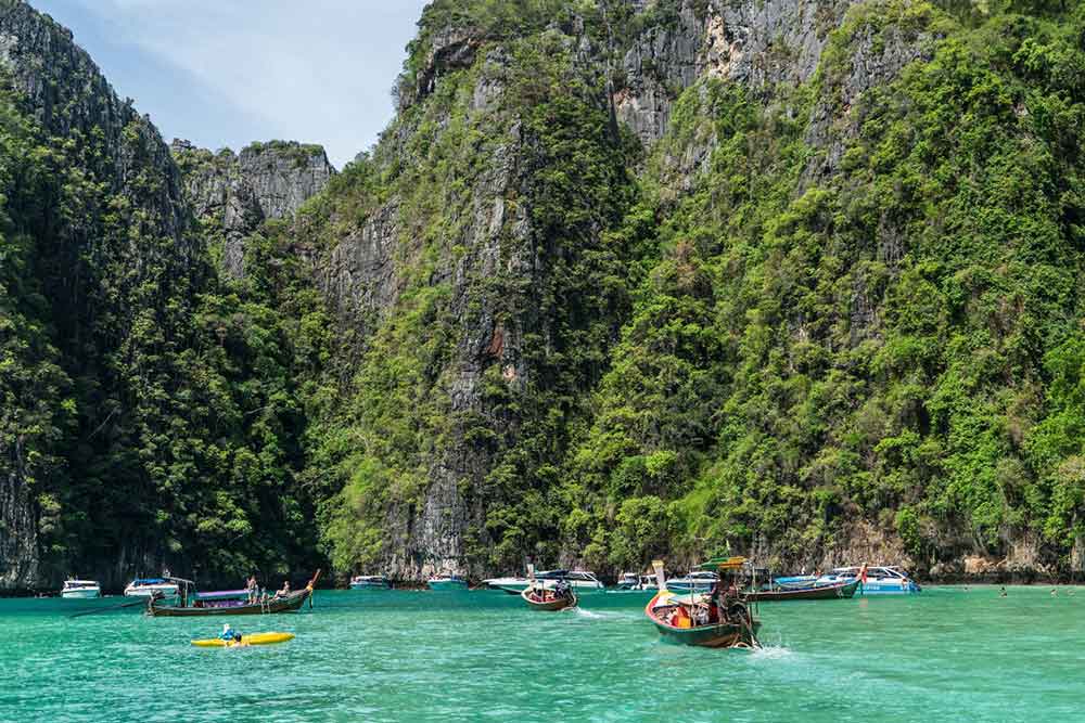 Boats sail through the middle of the beach, surrounded by towering, steep rock mountains at Phuket, Thailand - Phuket Thailand Pronunciation
