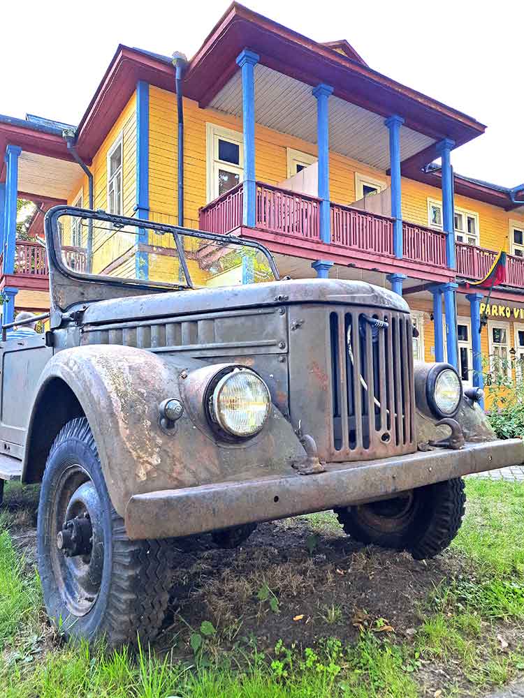 Druskininkai in Lithuania with an image on a rusty dark green jeep infront of a yellow, red and blue soviet house.