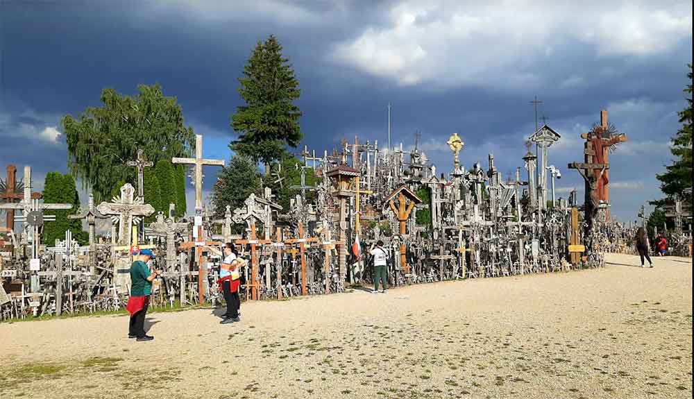 The Hill of Crosses featuring hundreds of crosses in different sizes - the sky is a dark grey and there are a few people in the foreground.