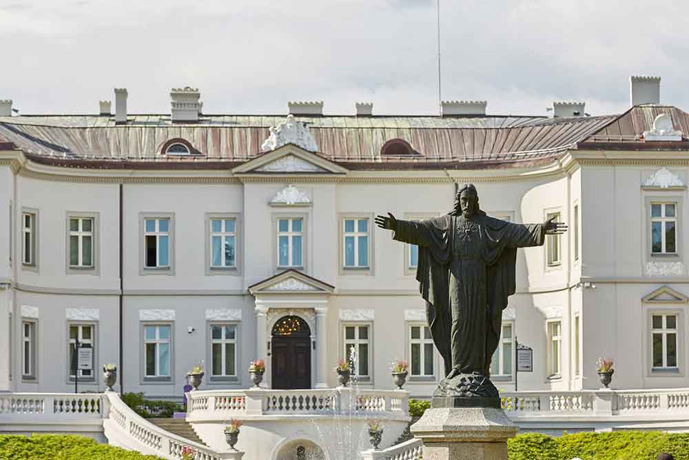 Palanga Amber Mueum a large white palacelike building with a statue of Jesus in the forgrouns. There are pots of flowers dotted around. 
