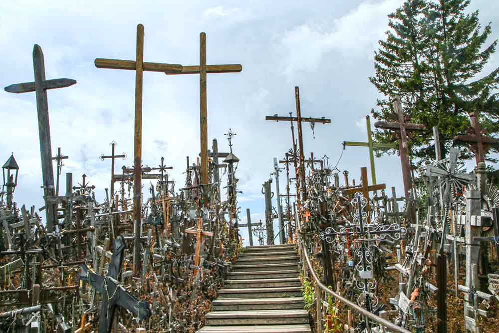The Hill of Crosses featuring hundreds of crosses in different sizes - the sky is a light grey and there are steps leading up the middle - there are hundreds of crosses on each side. 