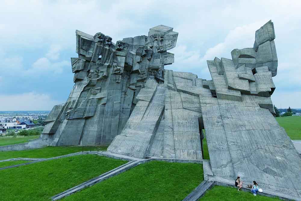 Ninth Fort Monument is an angualr concreet struture parts of the building look like stylised faces and hands or fists. It stis on a green lawn.  