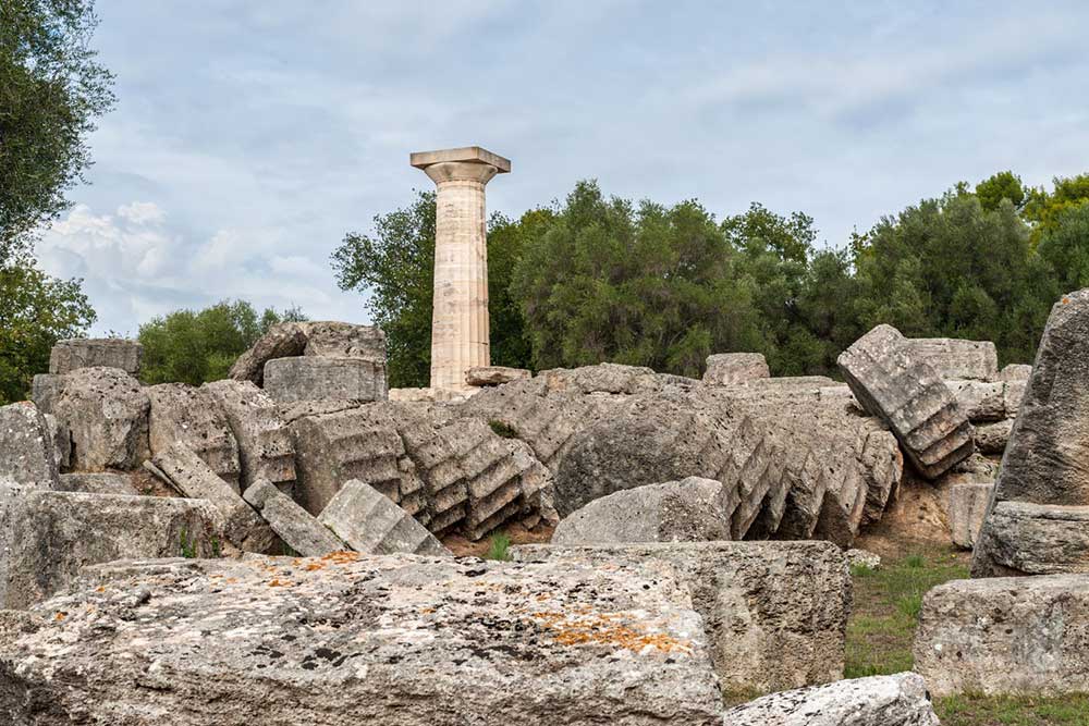 Is Peloponnese Worth Visiting? 15 Reasons to Visit the Peloponnese Region, Greece 3 The ruins of ancient Olympia in Greece. A single column stands amoungst fallen columns.
