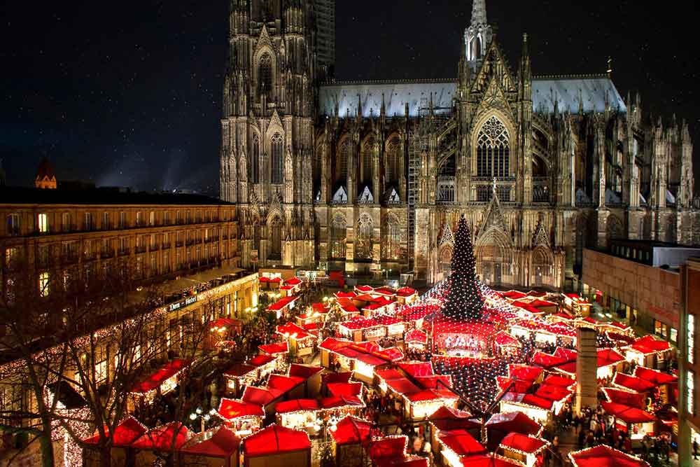 night time view of Cologne Cathedral Christmas Market with red roofs of buldings in front of the cathedral. 