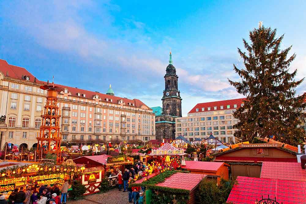 Striezelmarkt, Dresden with a christmas market in a town square. There is a christmas tree in the forground and a tower in the background. 