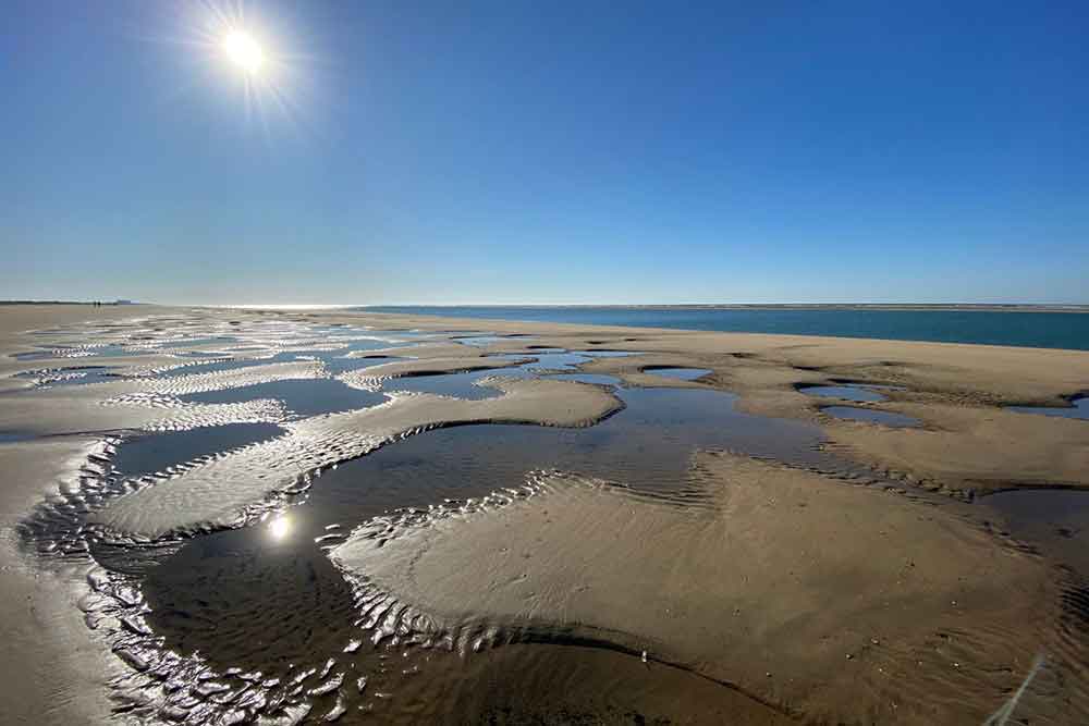 Lowtide at El Portil beach, with a wide flat beack and puddles left by the sea. The sea is in the distance. 