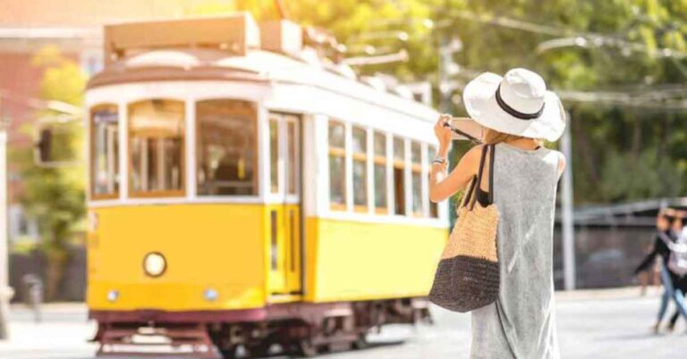 A woman wearing a grey dress with a white hat and straw bag photographing a yellow tram in lisbon. This is the featured image for an article to help you figure out how many days in spain and portugal you need.