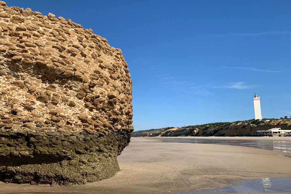 In the forground is a large boulder of an old buidling with a small wite square lighthouse in the background. This is Matalascañas beach, then closest Beach to Seville.