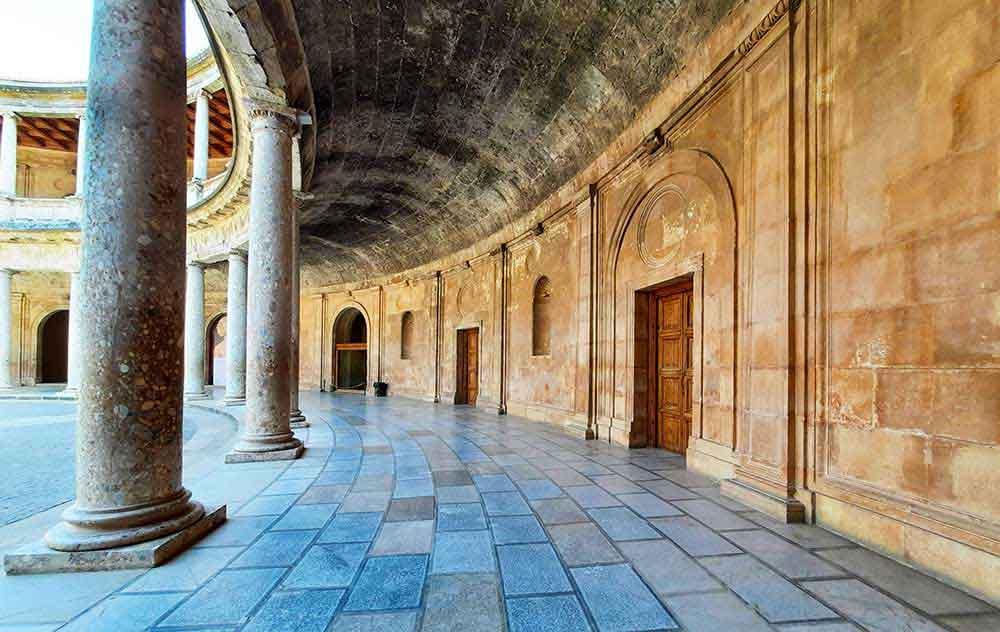 The curved alcove of Palace of Charles V in Alhambra with a grey marble floor, dany coloured walls and columns on the innder edge. 