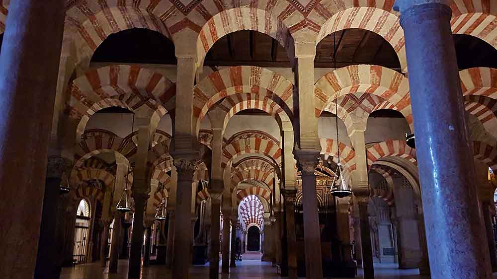 Inside the mosque-cathedral of Cordoba with row after row of arched columns. The arches are alternating red and yellow brick.