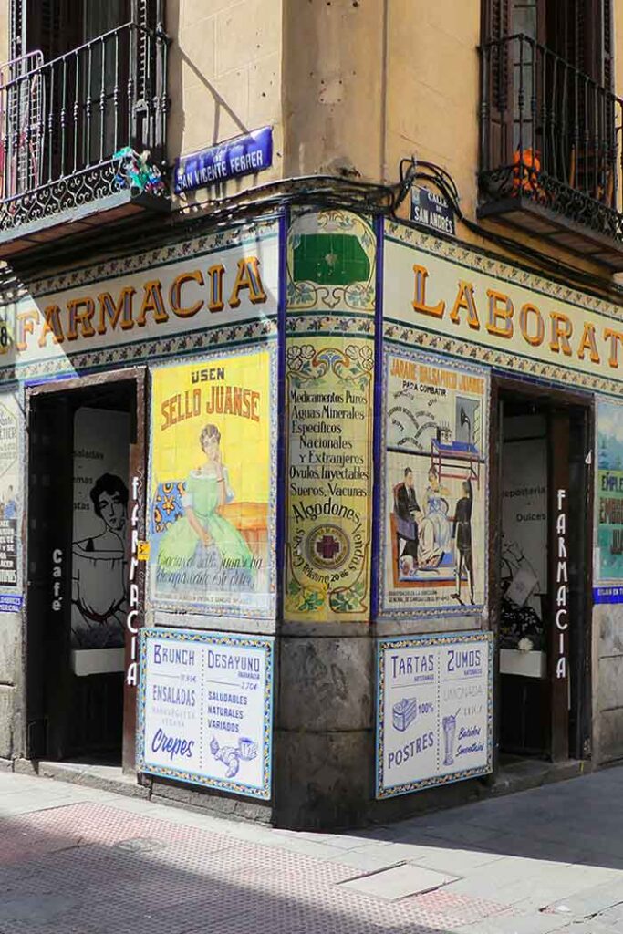 Corner of a building in Malasaña District with old advertisment tiles on it. Tis one says "farmacia" and has images of old posters selling medicine from a bygone era. Today it houses a cafe called "cafe farmacia".