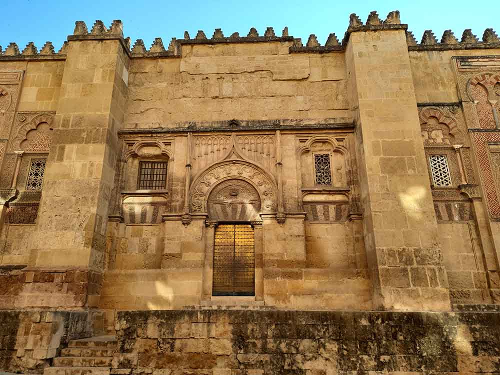 The Best Cordoba in One Day Itinerary 1 View of a side entrance of the Mezquita in Cordoba. An arabic influenced desing over a gold door.