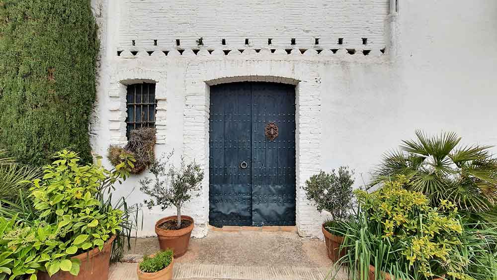 Best Montserrat Tour from Barcelona (With Tapas + Winery Visit) 7 A wooden blue door at Finca Ca n'Estella in a white washed wall surrounded by plants.
