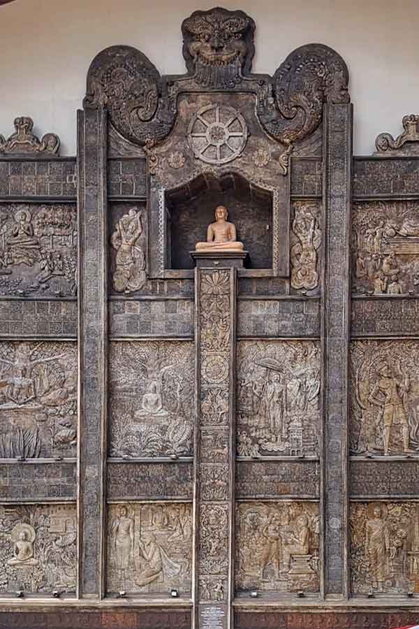 One of the walls at Gangaramaya Temple, Colombo. It features carvings in wood of Buddha as well as  statue of Buddha at the top.