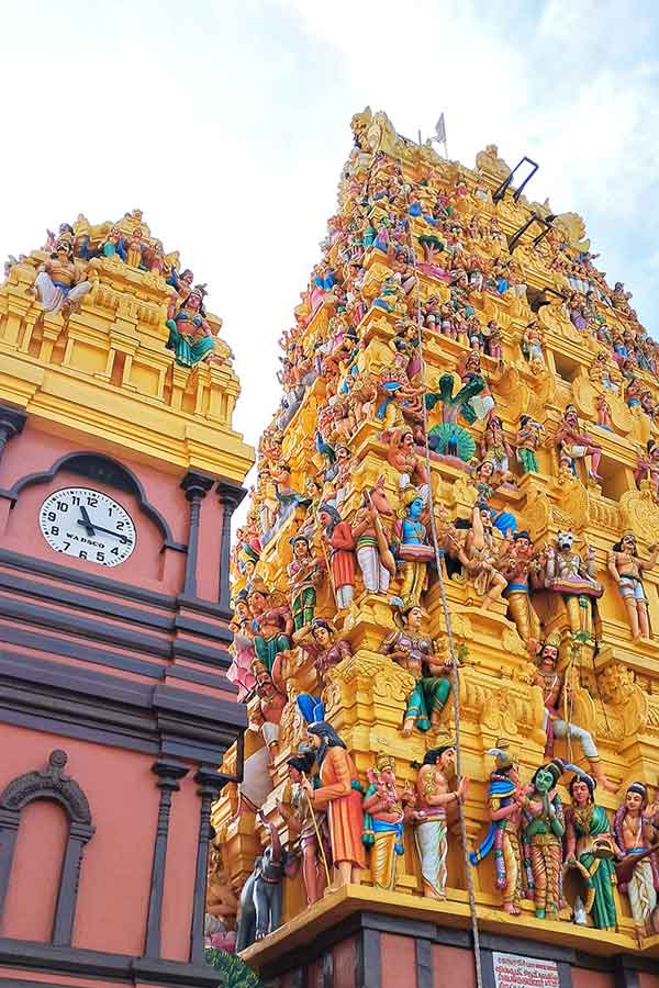 The colourful facade of the Sri Kailawasanatan Swami Temple, Colombo. The moslly yellow buiding is coverd in colour staures of Hindu dieties. There is a clock on a red building to the left side with more Hindu statues on top. 