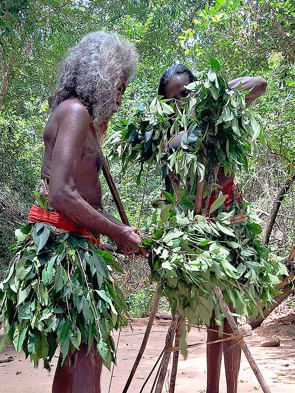 Two men wearing branches around their waist performing a traditional vedda ceremony.