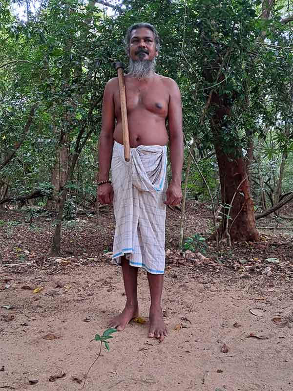 a Vedda man stood wearing a white cloth around his wast and an axe hanging over his right shoulder. 