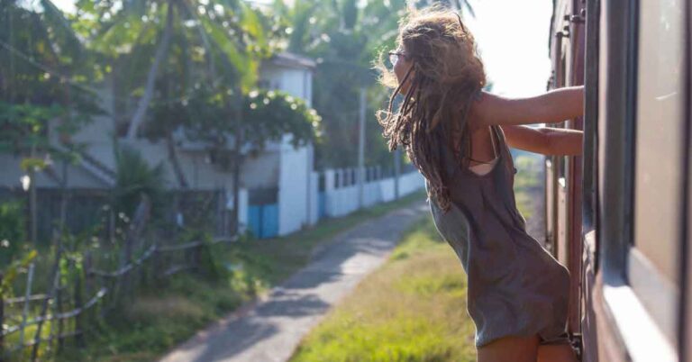A woman hanging out of a train in Sri Lanka wearing a long tshirt and shorts. Find out what to Wear in Sri Lanka in this article which includes a detailed Female Sri Lanka Packing List