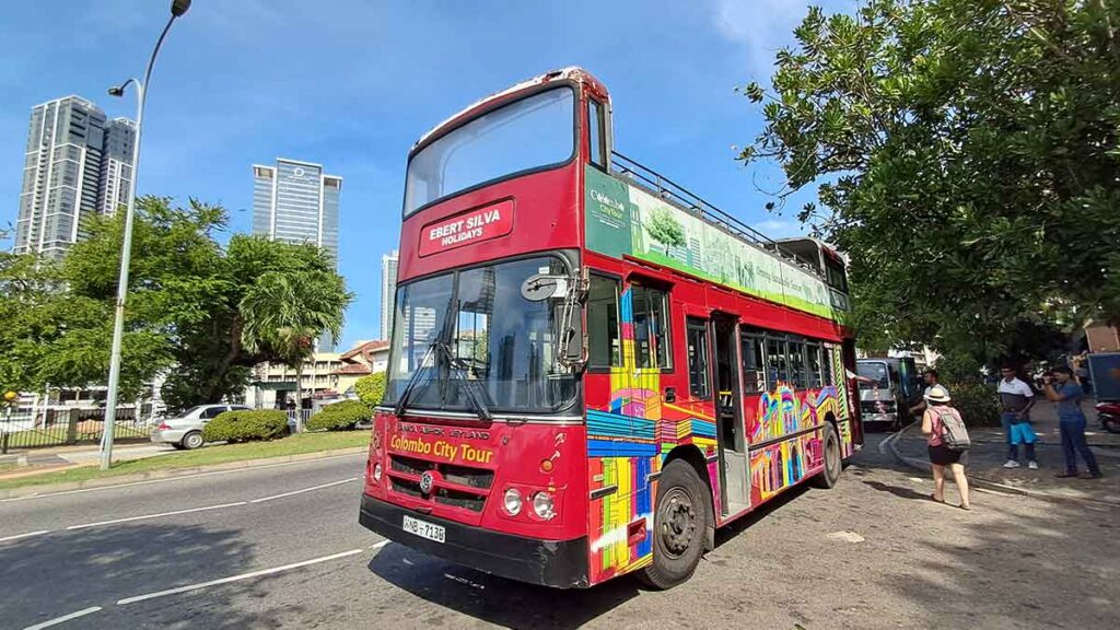 A red double decker bus with Colombo Cit Tour on the front and the sign that says "elbert silva holidays". There are people getting on the bus.