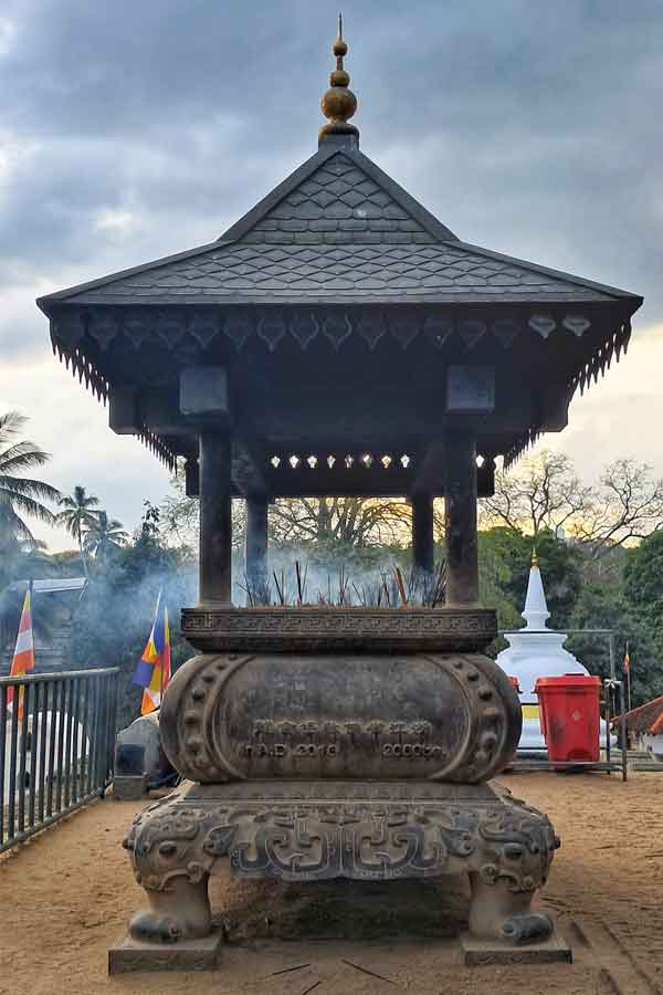 A shrine at Temple of the Tooth in the shape of a large casket with a triangular roof on top. There are insense burning and stood upright inside it.