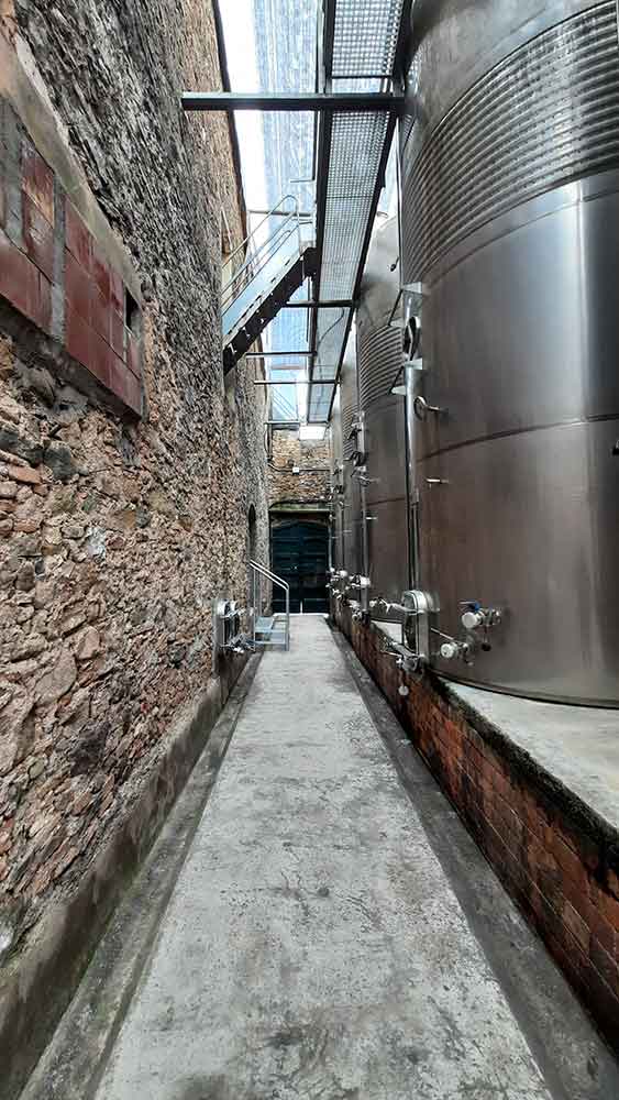 Best Montserrat Tour from Barcelona (With Tapas + Winery Visit) 16 Inside the winery with the large metal containers on the right, on the left is a brick wall which houses the old wine storage containers.