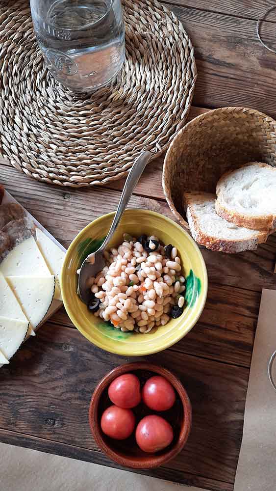 Best Montserrat Tour from Barcelona (With Tapas + Winery Visit) 18 various local foods. A bowl of bean salad, fresh break in a basket and tomatoes.