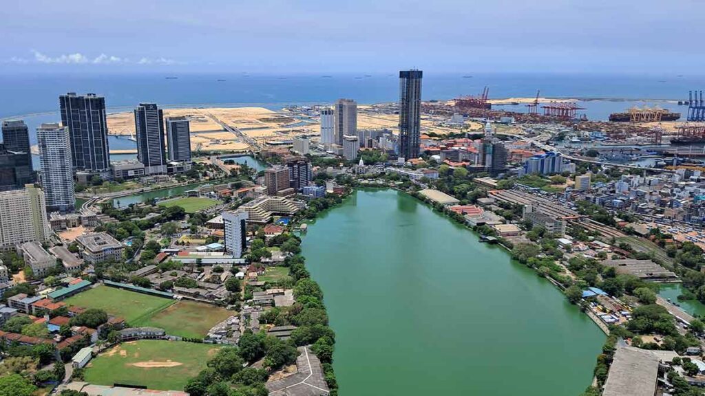 A view lookin gout over Colombo city from the Lotus Flower observation deck. A large lake in the middle is surrounded by buildings withthe port in the distance and the sea. 