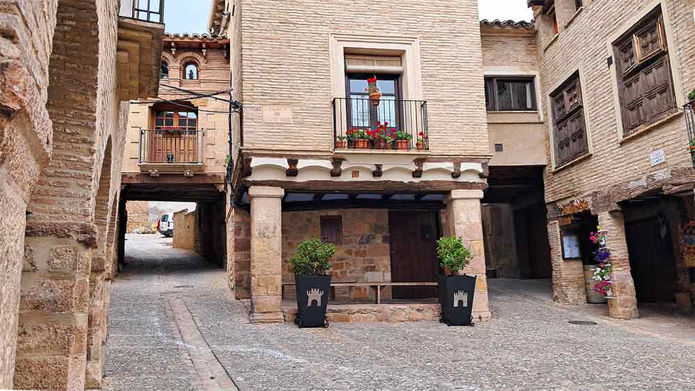 A peaceful medieval square in the village of Alquezar with charming stone buildings and potted flowers, offering a contrasting inland perspective from the coastal experiences typically associated with what San Sebastian is known for.