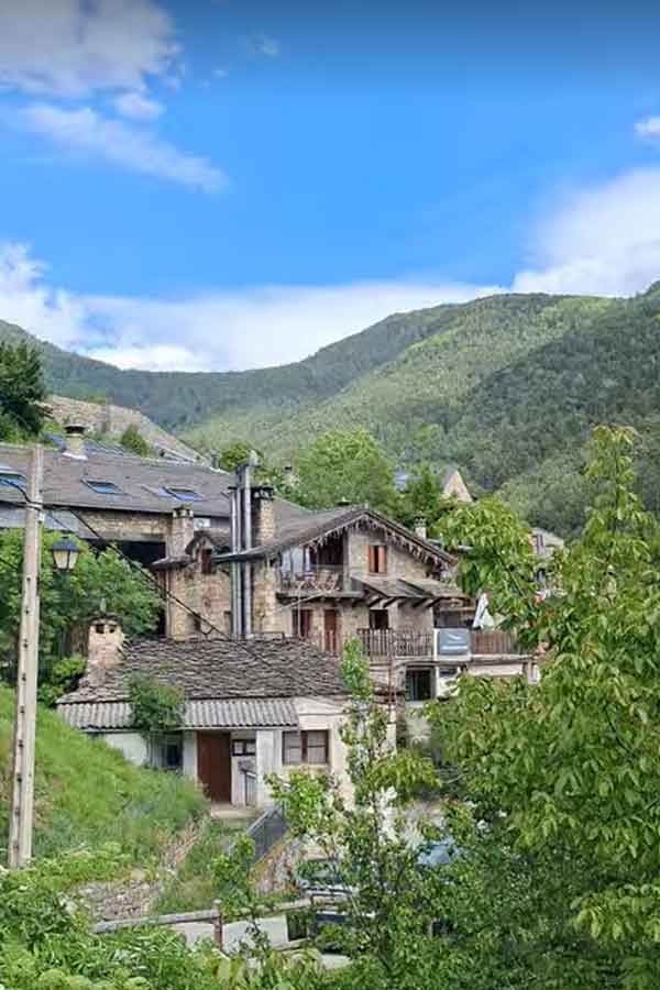 An Epic 5 Days Road Trip in Aragón Itinerary 18 The beautiful setting of the Balcon del Pirineo Restaurant. A chelet style house with chimkeys and multiple pitched roofs with small balconies with hills in the background.