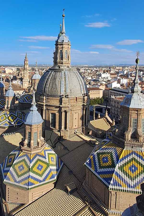Rooftop view of the Basilica of Our Lady of the Pillar. Some of the domes have colourful tiled patterns with a blue, yellow. green and white diamond design.
