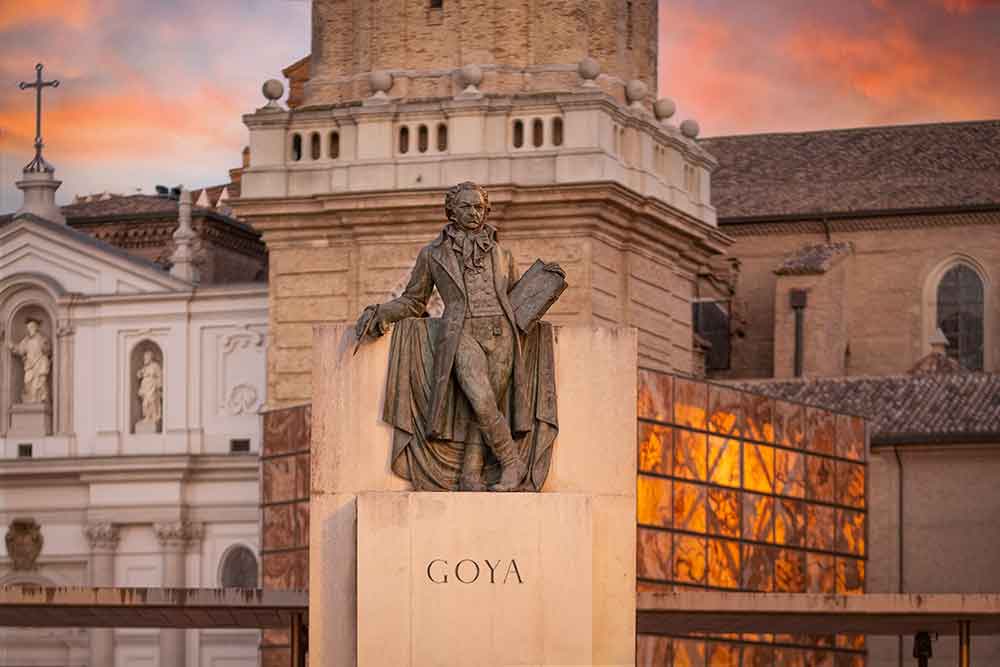 A statue of the artist Goya in the centre of Zaragoza with old buildings in the background.
